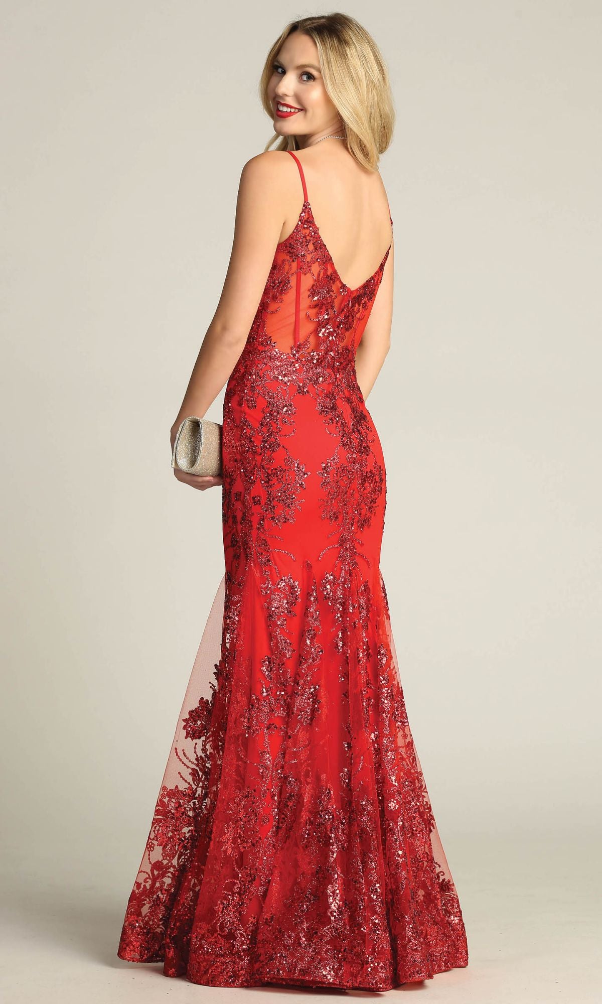Woman in the Chicas C813 Long Glitter-Print Prom Dress, a sleeveless, floor-length mermaid gown, holds a silver clutch and glances over her shoulder against a plain background.